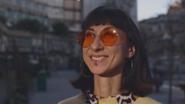 Meşgul bir caddede kameraya bakıp gülümseyen neşeli bir kadının yakın çekimi. Mutlu kız şık giyinir.