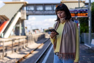 Tren bekleyen genç bir kadın. Telefonundaki uygulamayı kullanarak tren tarifesini kontrol eden bir yolcu. Tren istasyonunda bir kız..