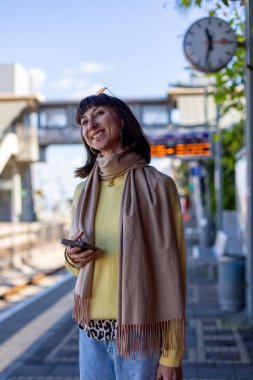 Tren bekleyen genç bir kadın. Telefonundaki uygulamayı kullanarak tren tarifesini kontrol eden bir yolcu. Tren istasyonunda bir kız..