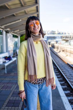 Şık bir kız istasyonda tren bekliyor. İstasyonda piercing takan ve şık güneş gözlüklü bir kızın portresi. Bir toplu taşıma yolcusu.