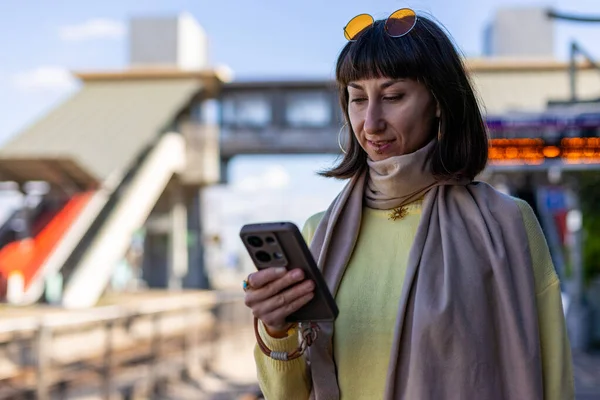 Genç bir kadın tren beklerken sosyal medya hesaplarını karıştırıyor. Yolcunun biri telefonundaki uygulamayı kullanarak tren tarifesini kontrol ediyor. Tren istasyonunda bir kız..