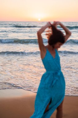 Elbiseli mutlu genç kız sahilde yürüyor. Mutlu kadın. Yumuşak odaklanma ve uzun deklanşör hızı. Bulanık hareket.