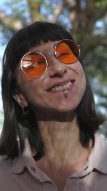 dikey video. Güneş gözlüklü mutlu bir kadının yüzü. Komik bir şakaya gülen bir insanın gülümsemesi ve duyguları. Kız gülümsüyor..