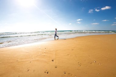 Kumsalda gülümseyen mutlu bir kadın. Güzel genç bir kadın boş bir sahil boyunca yürüyor. Mutlu bir kız yaz tatilinde beyaz kumlu bir plajda gezinir. Romantik ruh hali.