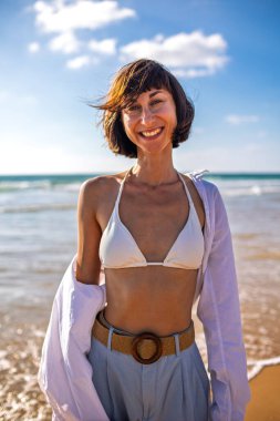 Plajda hasır şapkalı güzel bir kadının portresi, geniş bir gülümsemeyle kameraya bakıyor. Romantik bir ruh hali içindeki bir kızın çekici, gülümseyen yüzünün yakın çekimi..