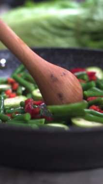 Dikey video. Kızartma tavasında karıştırılan yiyeceklerin yakın çekimi. Sağlıklı beslenme. Akşam yemeğini hazırlıyorum..