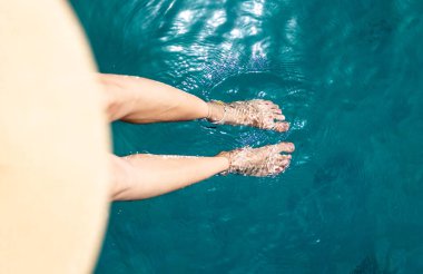 Yaz havası. Güzel ince bacakları olan bir kadın yaz güneşinin tadını çıkarırken, şapkalı bir kadın bacaklarını turkuaz suya daldırıyor. Bir kız dinleniyor..