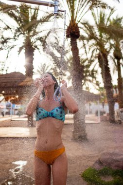 Yaz havası. Güneşli bir günde, plajdaki lüks bir otelde mayo giymiş esmer, beyaz bir kadın ferahlatıcı bir tropikal duş alıyor. Mayolu kız..