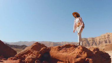 Sırt çantalı bir kadın kuru kumlu arazide yürüyor, çölün çevresini keşfediyor. Gezinti ve yürüyüş.