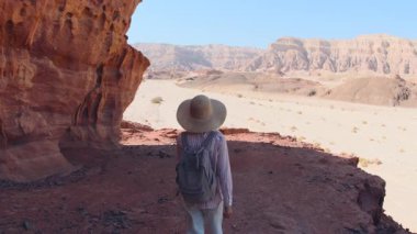 Sırt çantalı bir kadın kuru kumlu arazide yürüyor, çölün çevresini keşfediyor. Gezinti ve yürüyüş.