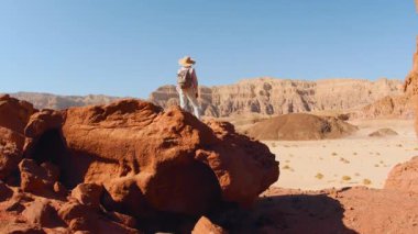 Sırt çantalı bir kadın uçurumun kenarında duruyor ve çöl çevresini inceliyor. Çöl yürüyüşü ve yürüyüş. Maceralar