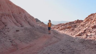 Sırt çantası ve elinde harita olan bir çocuk çölde bir patika boyunca yürüyor. Aktif tatil. Gezinti ve yürüyüş.