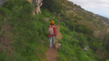 Sırt çantalı bir kız ormanda yürüyor. Turist gezisi konsepti. Genç, mutlu bir kadın dağ yolunda yürüyor. Arka.