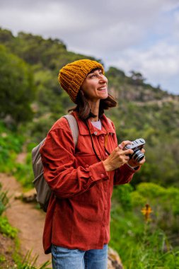 Kameralı bir kız. Bir kadın yürüyüş sırasında doğanın ve dağların fotoğraflarını çekiyor. Bir kadın fotoğrafçı sosyal medya için içerik çekiyor. Aktif eğlence ve spor.