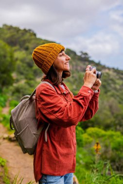 Elinde fotoğraf makinesi olan mutlu bir kızın portresi. Bir kadın dağlarda yürüyüş yapıyor ve yolculuğun tadını çıkarıyor. Sırt çantası ve kamerası olan bir kadın. Aktif eğlence ve spor.