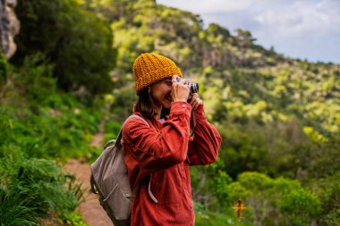 Elinde fotoğraf makinesi olan mutlu bir kızın portresi. Bir kadın dağlarda yürüyüş yapıyor ve yolculuğun tadını çıkarıyor. Sırt çantası ve kamerası olan bir kadın. Aktif eğlence ve spor.