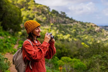 Kameralı bir kız. Bir kadın yürüyüş sırasında doğanın ve dağların fotoğraflarını çekiyor. Bir kadın fotoğrafçı sosyal medya için içerik çekiyor. Aktif eğlence ve spor.