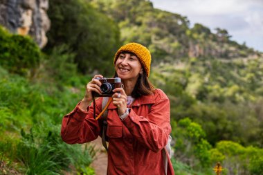 Kameralı bir kız. Bir kadın yürüyüş sırasında doğanın ve dağların fotoğraflarını çekiyor. Bir kadın fotoğrafçı sosyal medya için içerik çekiyor. Aktif eğlence ve spor.