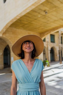 Şehirde saman şapkalı güzel bir genç kadının portresi. Yaz tatili boyunca gülümseyen neşeli genç bir kadın. Mutlu kız güneşten zevk alıyor.