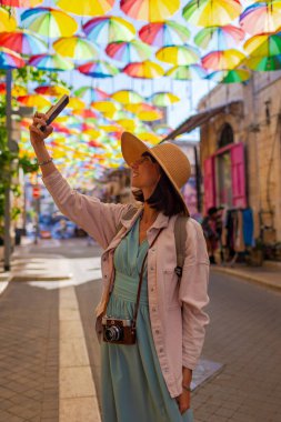 Kadın gezgin, tarihi bir şehirde telefonuyla tarihi işaretlerin fotoğraflarını çekiyor. gökyüzü şemsiyesi Kız içerik yaratır.