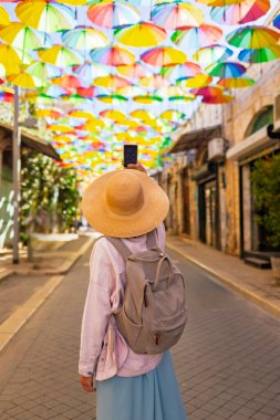 Gezintiye çıkmış kız turist elinde şemsiyelerle sokakta duruyor ve fotoğraf çekiyor. Şemsiye. kız içerik yaratır.