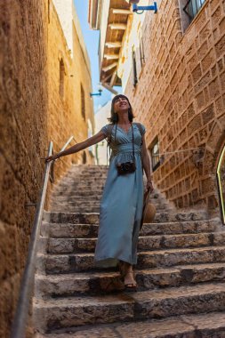 Açık havada yürüyorum. Neşeli gülümseyen stil sahibi kadın turist. Eski şehrin sokaklarında yürüyen bir gezgin. Seyahat ve tatil.