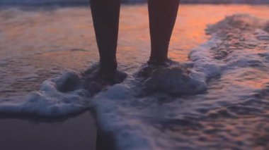 Sahilde bir kız. Suda çıplak ayaklı bir kadının yakın çekimi. Gün batımında bir kadın sahilde duruyor. Aşk ve aşk