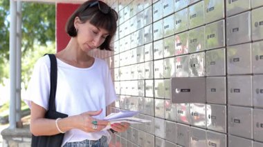 Sokakta posta kutusunu açıp kontrol eden genç bir kadının yakın çekimi. Yan görüş. Postası olan kız.