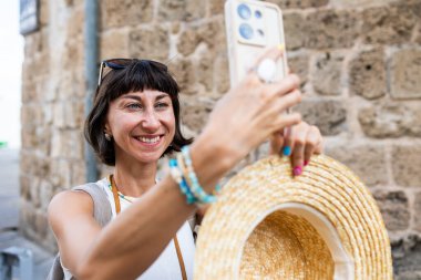 Arap ülkesindeki eski şehrin caddesinde yürüyen neşeli, güler yüzlü bir kadın. Şık gezgin sosyal ağlar için manzara fotoğrafları çekiyor. Telefonu olan kız..