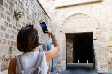 Arap bir ülkede, eski şehrin caddelerinde yürüyen ve sosyal ağlar için manzara fotoğrafları çeken neşeli, güler yüzlü bir kadın. Telefonlu bir kız. Mutlu turist.