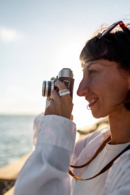Kız fotoğraf çekiyor. Güzel bir turist hafta sonu tatili boyunca deniz manzarasının keyfini çıkarıyor ve film kamerasıyla fotoğraf çekiyor. Kameralı kız. Hobi ve eğlence konsepti.