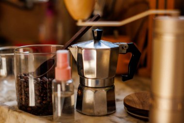 Evdeki masada Moka pot var. Kahve yapma konsepti. Moka demliği, fasulye spreyi, kahve öğütücü, mutfak masasının üzerinde duran bir kavanoz kahve çekirdeği. Kahve yapmak için gerekli malzemeler.