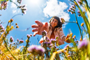 Mutlu bir kız. Genç bir kadın parlak bir gökyüzü altında yemyeşil çiçeklerin arasından rengarenk çiçekler topluyor, doğanın huzurunun tadını çıkarıyor. Çiçek toplama.