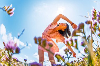 Çiçek tarlasında elini kaldıran ve anın tadını çıkaran güzel bir kadın. Yaz havası. Yazlık elbise giymiş ince bir kız. Çiçeklerin arka planında bir kız.