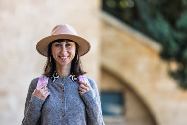 Keyfi yerinde bir kızın fotoğrafı, şık kıyafetler giyiyor, sırt çantası taşıyor, şehir caddesinde yürüyor. İsrail 'de seyahat. Şehirde sırt çantalı bir kız.