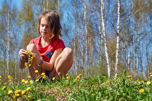 Schoolgirl making wreath of dandelions outdoors — Stock Photo, Image