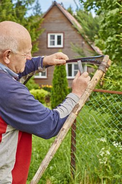 Ağarmış adam tırpan yaz evinin önünde keskinleştirme 