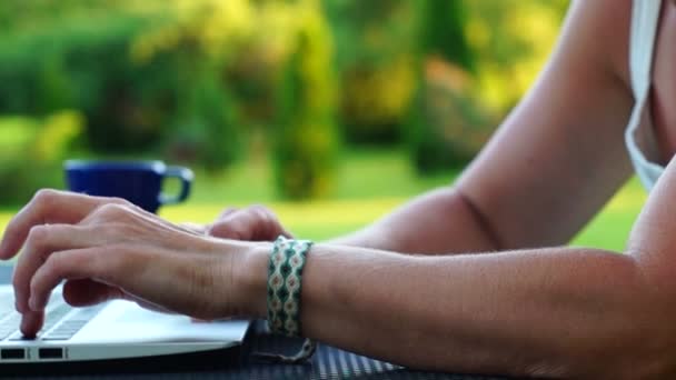 在绿色的花园里的一台笔记本电脑的键盘上打字的女性手 — 图库视频影像