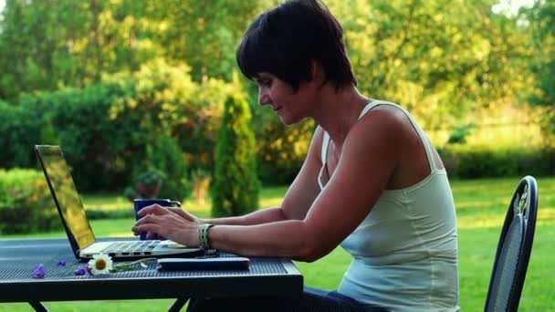 Mulher de meia-idade agradável trabalhando em um laptop ao ar livre — Vídeo de Stock