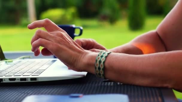 Female hands typing on the keyboard of a laptop in the green garden — Stock Video