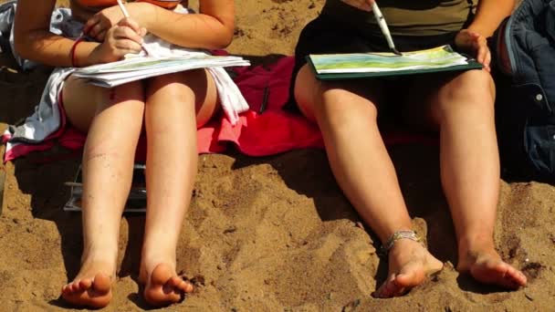 Босоногі дівчата малюють пейзажі з акварелями, що сидять на пляжі — стокове відео