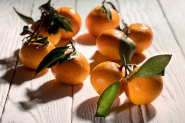 Taze mandalinalar, gölgeli sert ışıkla aydınlatılan beyaz tahta tahtalarda yatıyor.