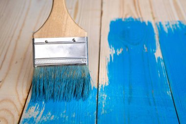 Arka planda mavi boya fırçasıyla ahşap kaplamaları boyuyor. Ön manzara. Resim işe yarıyor. Boşluğu kopyala.