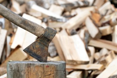 Ahşap saplı eski paslı baltayla arka planda yakacak odun yığını var. Odun kesme işi.