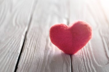 Beyaz desenli ahşap tahtaların üzerinde duran arkadan aydınlatılmış pembe yünlü bir kalple Sevgililer Günü kartı. Boşluğu kopyala.