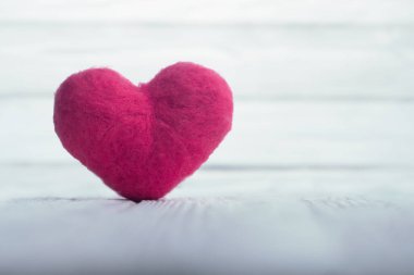 Pembe yünlü kalp arka planda bulanık beyaz tahtaları olan beyaz desenli tahta tahtalarda duruyor. Boşluğu kopyala.