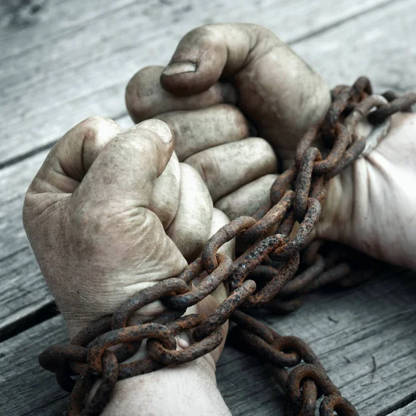 Male hands chained with old rusty chain on the wooden boards. — Stock Photo, Image