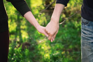 Yaz günbatımında arka planda yeşil çimlerle el ele tutuşan genç çift.