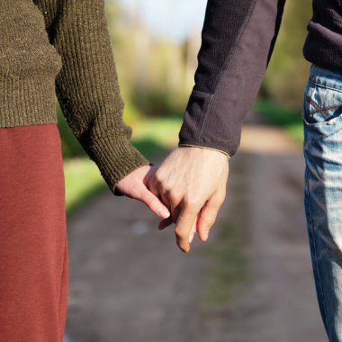 Yazın gün batımında arka planda kırsal bir yolda el ele tutuşan genç çift.