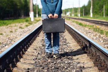 Bir kadın el ele tutuşmuş demiryolunda duruyor. Yaz sabahı eski bir bavul.
